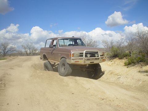 1989 Ford Bronco - This 1989 Ford Bronco navigates a challenging dirt track under a partly cloudy sky.
