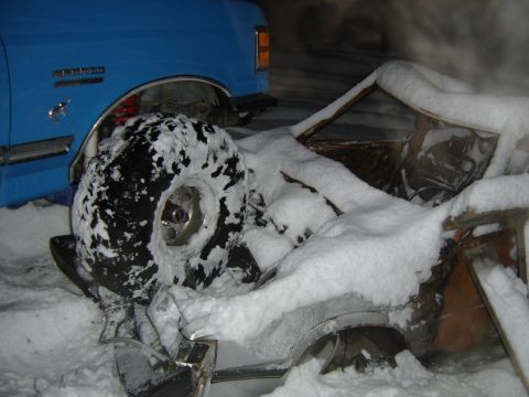 1988 Ford Bronco - Night shot of a blue Ford Bronco with running-horse emblem and red-painted rear suspension, its rear wheel arch empty while a snow-covered…