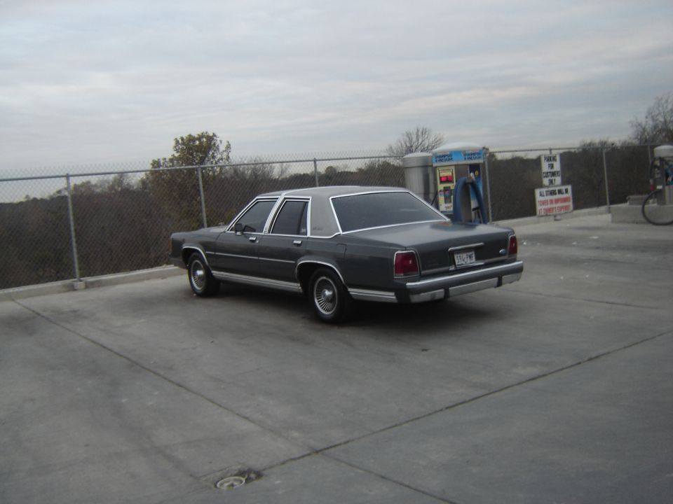 Dark sedan parked at a gas station with a chain-link fence behind it