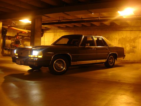 1988 Ford Crown Victoria LTD - A 1988 Ford Crown Victoria LTD sedan is captured in a 3/4 front view, parked in a dimly lit garage with artificial lighting.