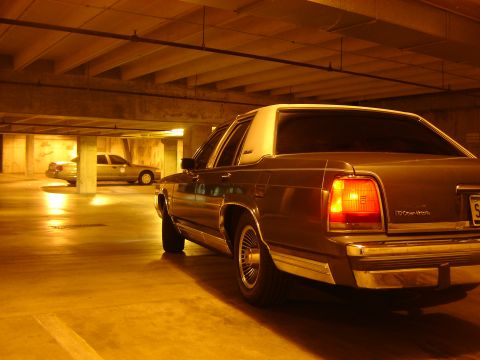 1988 Ford Crown Victoria LTD - A brown sedan with a white roof sits in a dimly lit parking garage, with another car in the distance.