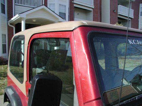 1998 Jeep TJ - A red Jeep Wrangler with a tan soft top is parked in front of an apartment building.