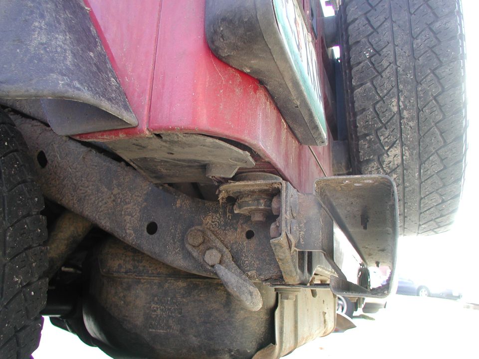 Close-up of a red Jeep Wrangler's rear bumper, showing the tire carrier and spare tire. The frame and suspension components are visible
