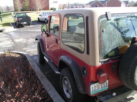 1998 Jeep TJ - A red and tan Jeep Wrangler is parked in a lot, with a black pickup truck and a silver sedan visible in the background.