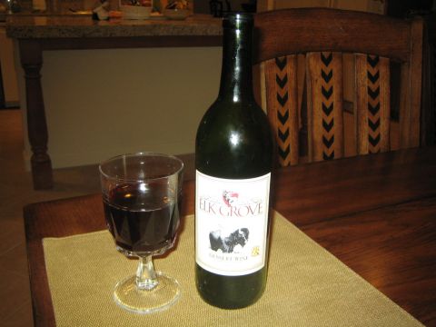 1968 Ford Mustang - A bottle of Elk Grove dessert wine sits next to a glass of red wine on a table, with a wooden chair in the background.
