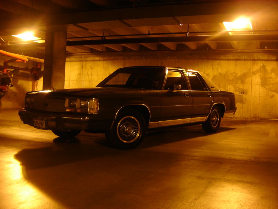 Dark sedan parked in a dimly lit garage, showing its front quarter view with chrome trim and wire wheels