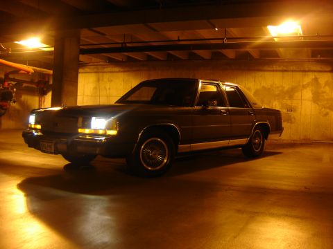 1988 Ford Crown Victoria LTD - A 1988 Ford Crown Victoria sits in a concrete parking garage under yellow lights.