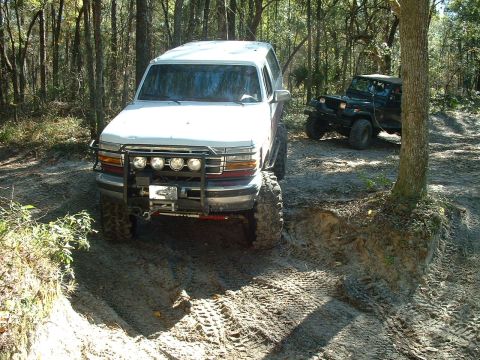 1995 Ford Bronco - Two off-road vehicles, a Ford Bronco and a Jeep Wrangler, navigate a muddy trail.