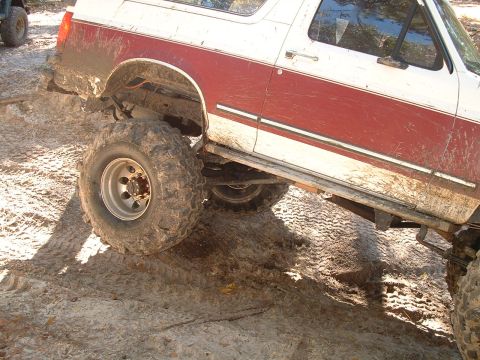 1995 Ford Bronco - This modified SUV is navigating a challenging off-road course, with one wheel significantly elevated.
