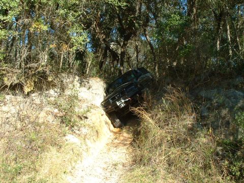 1995 Ford Bronco - A black 1995 Ford Bronco is captured in a three-quarter front view as it maneuvers through a challenging off-road trail with steep embankme…