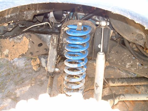 1995 Ford Bronco - The vehicle's suspension system, including a blue coil spring and shock absorber, is covered in mud and dirt.
