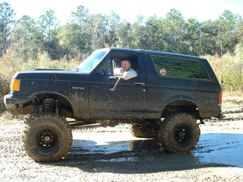 1995 Ford Bronco - Modified black Ford Bronco navigating a muddy off-road course.