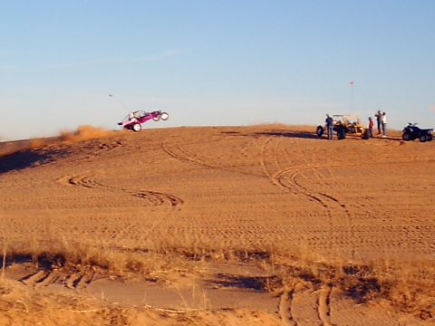 1991 Ford Bronco - A dune buggy takes flight over a sandy hill while other off-road vehicles and spectators watch.