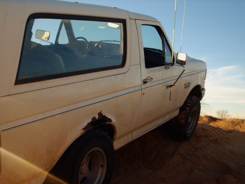 1991 Ford Bronco - 1991 Ford Bronco on a sand dune, with visible rust on the rear fender.