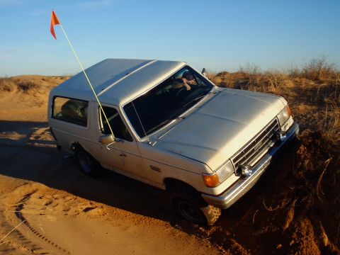 1991 Ford Bronco - This Ford Bronco is navigating a sandy terrain under a clear blue sky.