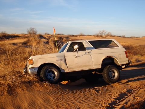 1991 Ford Bronco - A white 1987 Ford Bronco navigates a sandy terrain with an orange flag in the background.