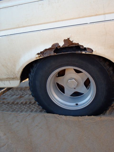 1991 Ford Bronco - The side of a 1991 Ford Bronco displays significant rust around the wheel well, with a star-patterned wheel visible.