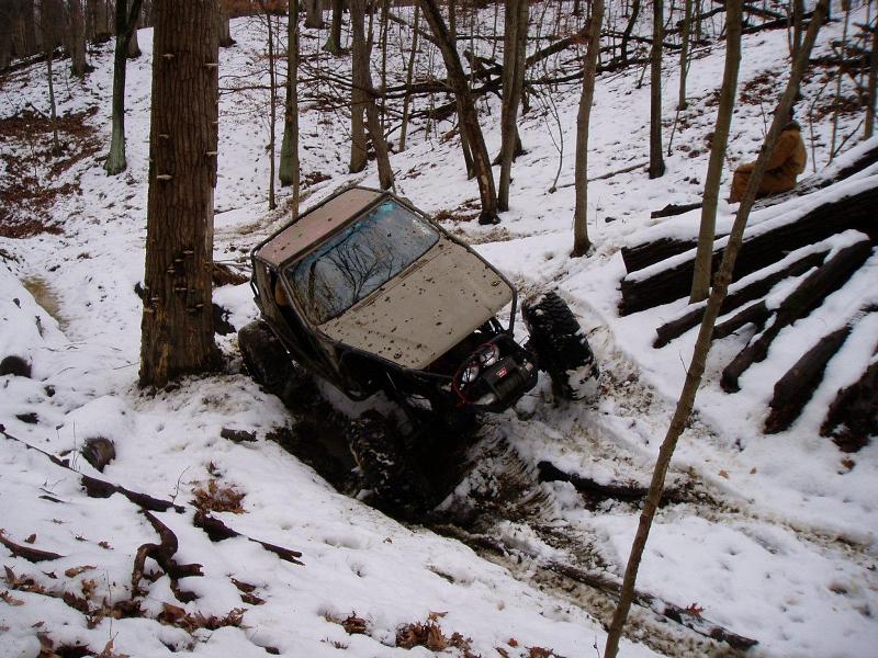 1992 Ford Bronco stuck in snow on a wooded trail, front right wheel off the ground