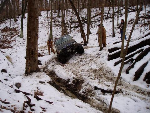 1992 Ford Bronco - A Jeep Cherokee XJ navigates a challenging snowy and muddy terrain with onlookers present.