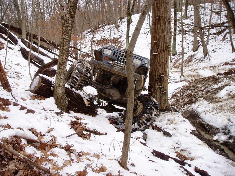 Off-road vehicle tilted on snowy hill with trees and logs