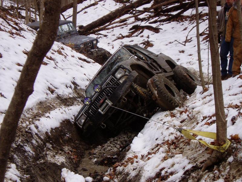 Two off-road vehicles stuck in a snowy, muddy ditch; one is tilted