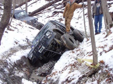 1992 Ford Bronco - Two off-road vehicles are stuck in a muddy, snowy ditch on a wooded slope.