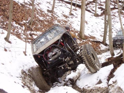 1992 Ford Bronco - A heavily modified off-road vehicle navigates a snowy, wooded trail with another vehicle visible in the background.