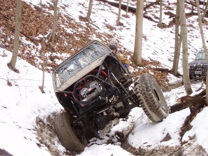 Modified off-road vehicle with roll cage and winch tilted in snowy terrain