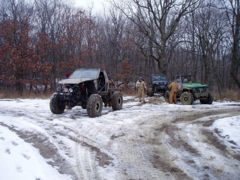 1992 Ford Bronco - Modified off-road vehicles are parked on a snowy path in a wooded area.