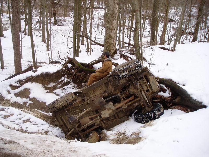 Overturned off-road vehicle in snowy woods with a person sitting on its side