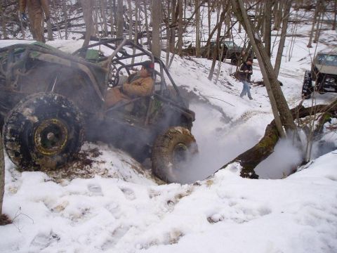 1992 Ford Bronco - A heavily modified off-road buggy with a roll cage tackles a snowy obstacle, with other vehicles visible in the background.