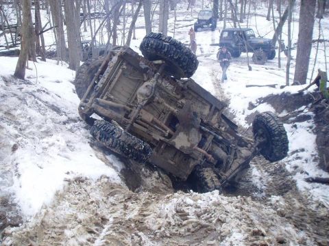 1992 Ford Bronco - An off-road vehicle is stuck and overturned in a snowy, muddy ditch.