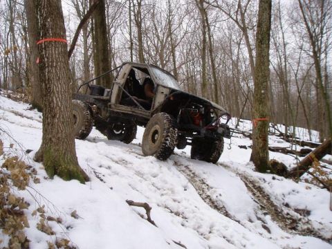 1992 Ford Bronco - This heavily modified off-road truck navigates a challenging snowy incline, its capabilities in a wooded environment.