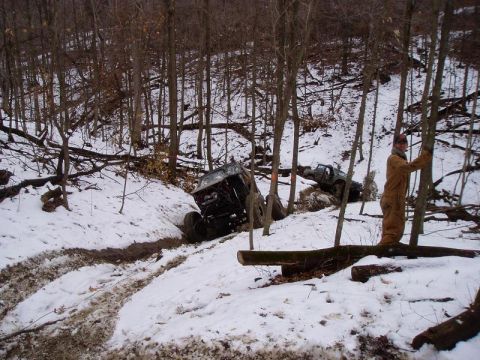 1992 Ford Bronco - Off-road vehicles stuck in a snowy wooded area, with a person standing nearby.