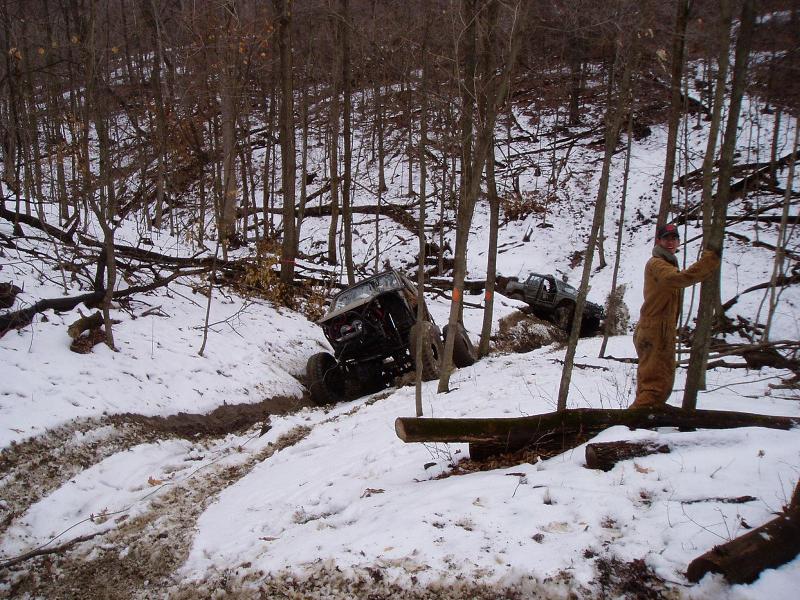 Two off-road vehicles stuck in a snowy ditch with trees and fallen logs around