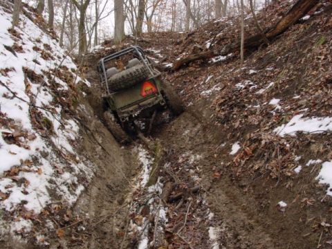 1992 Ford Bronco - An off-road vehicle navigates a treacherous, muddy incline with snow on the surrounding banks.