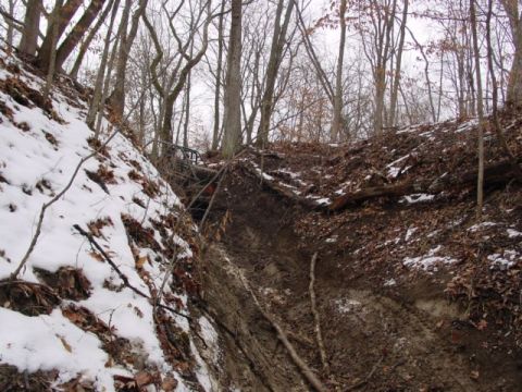 1992 Ford Bronco - An off-road vehicle navigates a challenging, muddy, and snowy ravine in a wooded area.