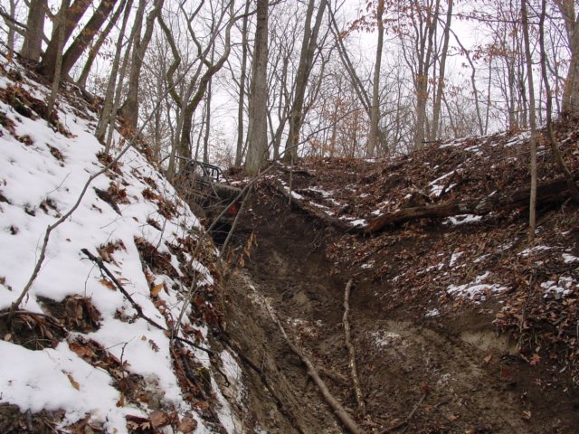 off-road vehicle stuck in a muddy, snowy ravine with trees all around