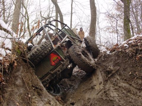 1992 Ford Bronco - An off-road vehicle is stuck in a muddy ditch, with a person observing from the side.