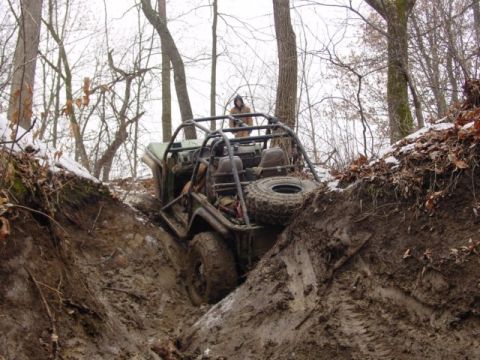1992 Ford Bronco - An off-road vehicle navigates a challenging muddy terrain, its tires deep in the mire.