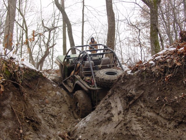 Off-road vehicle with roll cage stuck in a muddy ditch, spare tire visible