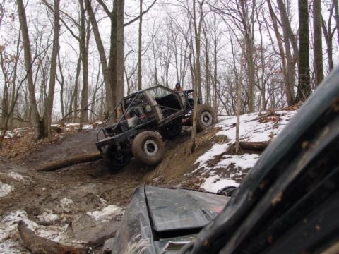1992 Ford Bronco - Modified off-road vehicle navigates a challenging muddy terrain in a wooded area.