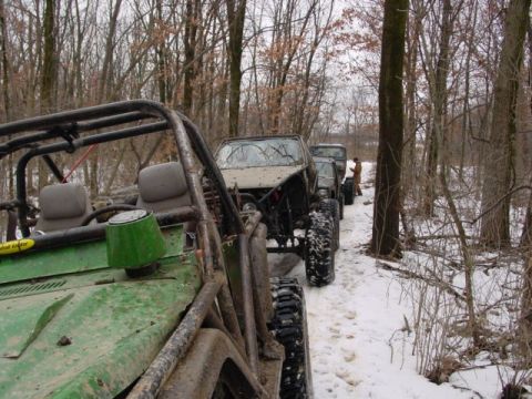 1992 Ford Bronco - A line of off-road vehicles navigate a snowy trail through a forest.