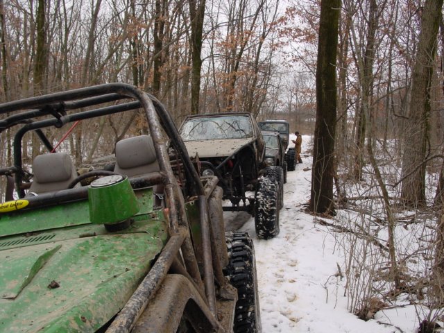 Several off-road vehicles lined up on a snowy path in a wooded area