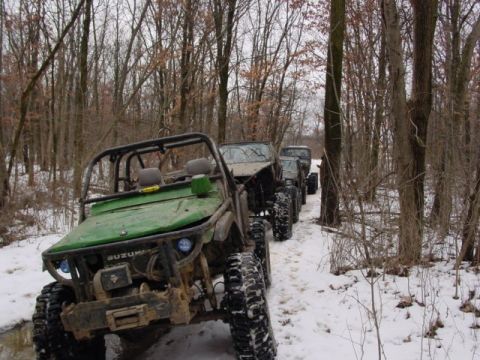 1992 Ford Bronco - A line of off-road vehicles navigates a snowy path through a wooded area.