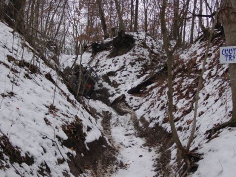 1992 Ford Bronco - An off-road vehicle is stuck in a snowy ditch on a wooded trail, with a sign for 'Coot Trail' visible.
