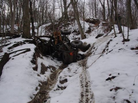 1992 Ford Bronco - An ATV is stuck and tipped on its side on a snow-covered trail surrounded by trees.
