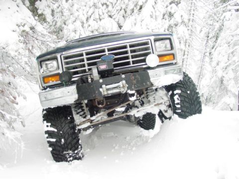 1986 Ford Bronco - Ford Bronco with large tires and winch navigates deep snow in a wooded area.