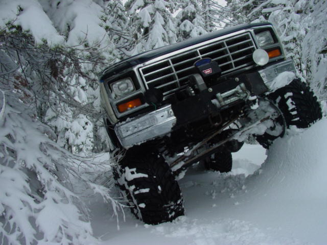 Dark blue 1986 Ford Bronco driving through deep snow with winch visible