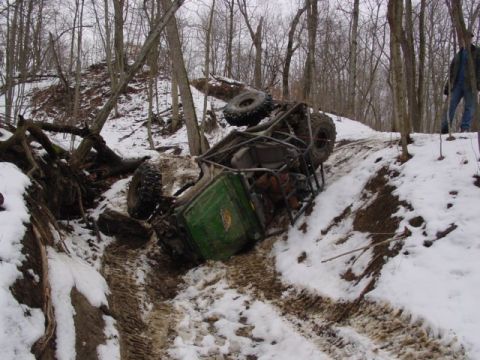 1992 Ford Bronco - An off-road vehicle has tipped over on a snowy trail, with a person standing on a nearby embankment.